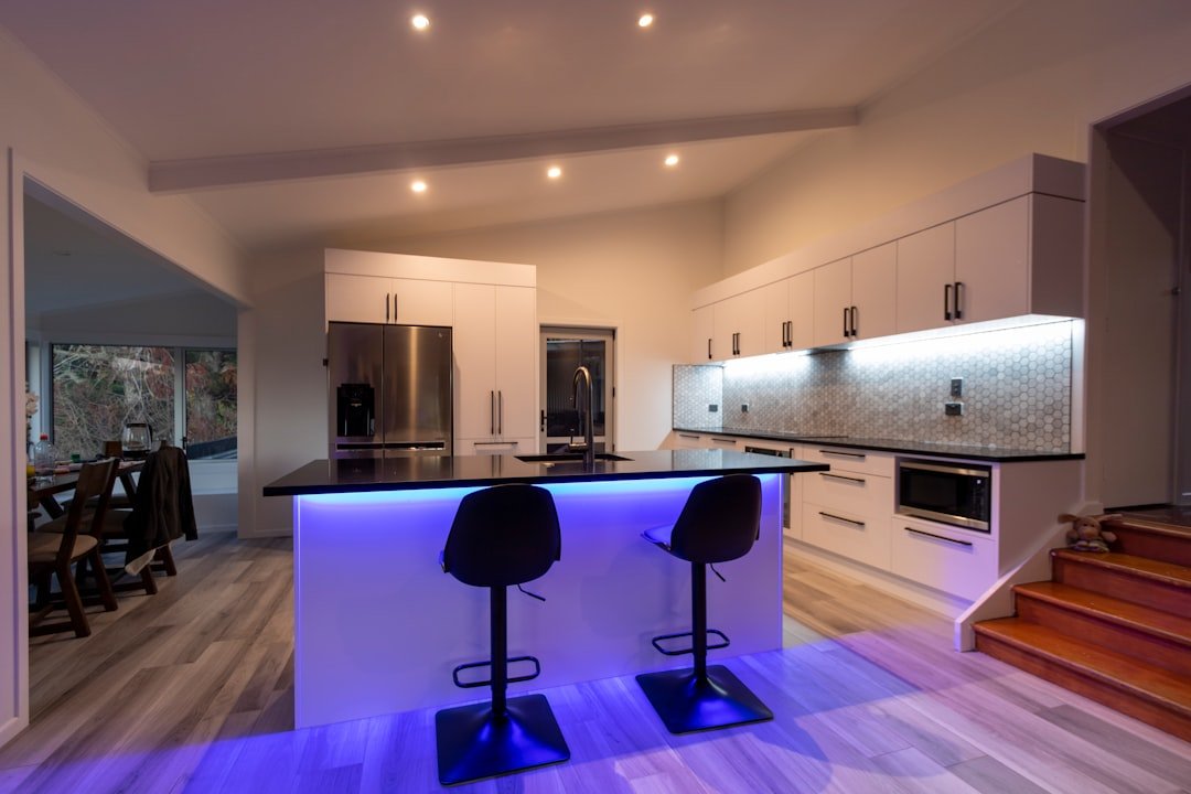 A modern white kitchen with led strip lighting, tiled wooden like flooring and a tile splashback